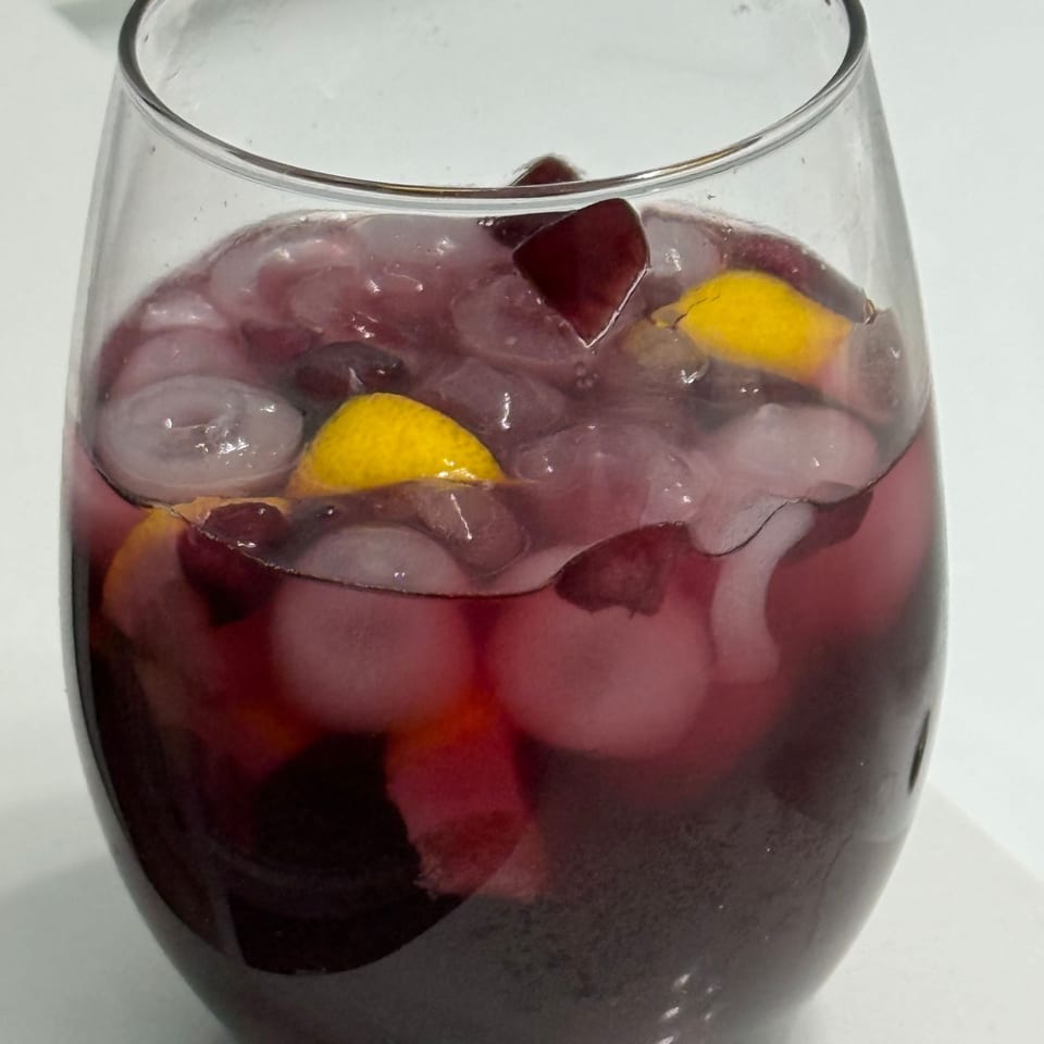 A glass filled with dark red fruit punch, ice cubes, and visible lemon and berry pieces.