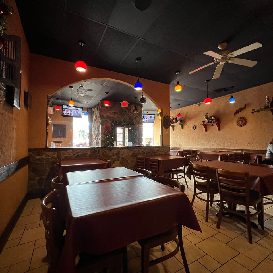 Warmly lit restaurant dining room with colorful pendant lights, covered tables, stone accents, wall decorations, and two diners.