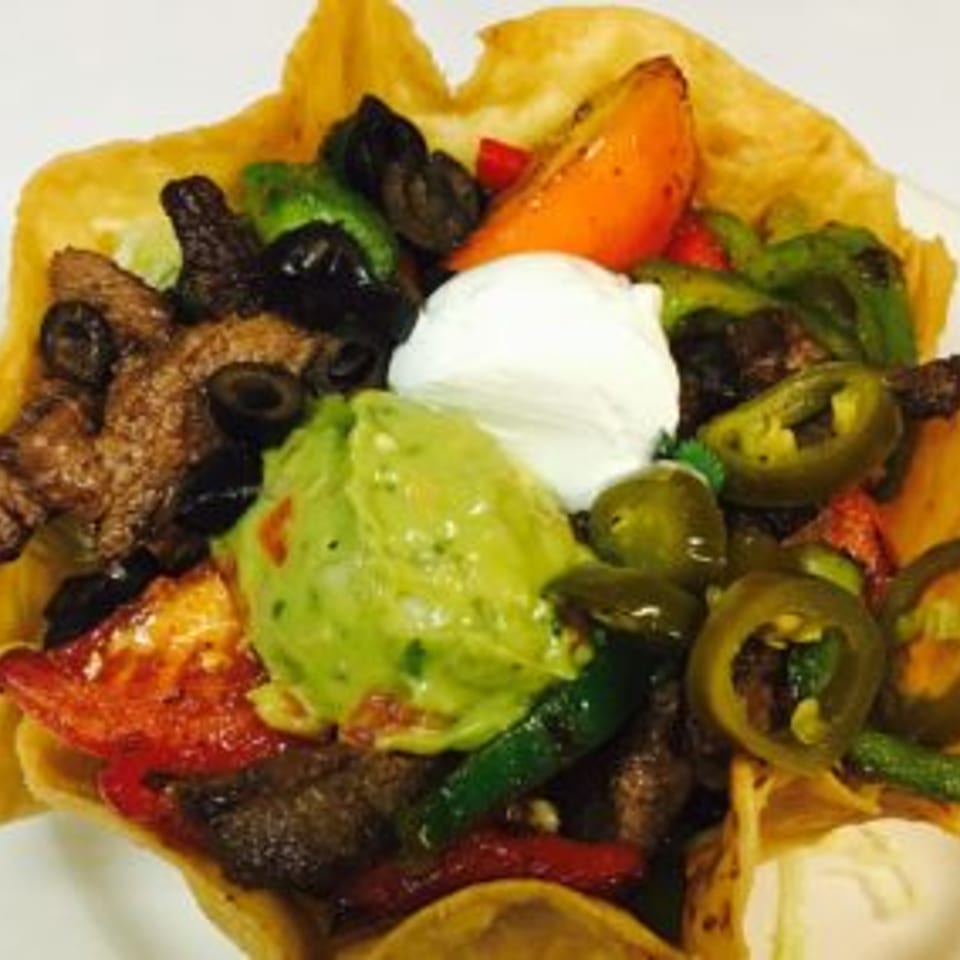 Taco topped with grilled steak, guacamole, sour cream, black olives, jalapeños, roasted vegetables, and melted cheese.