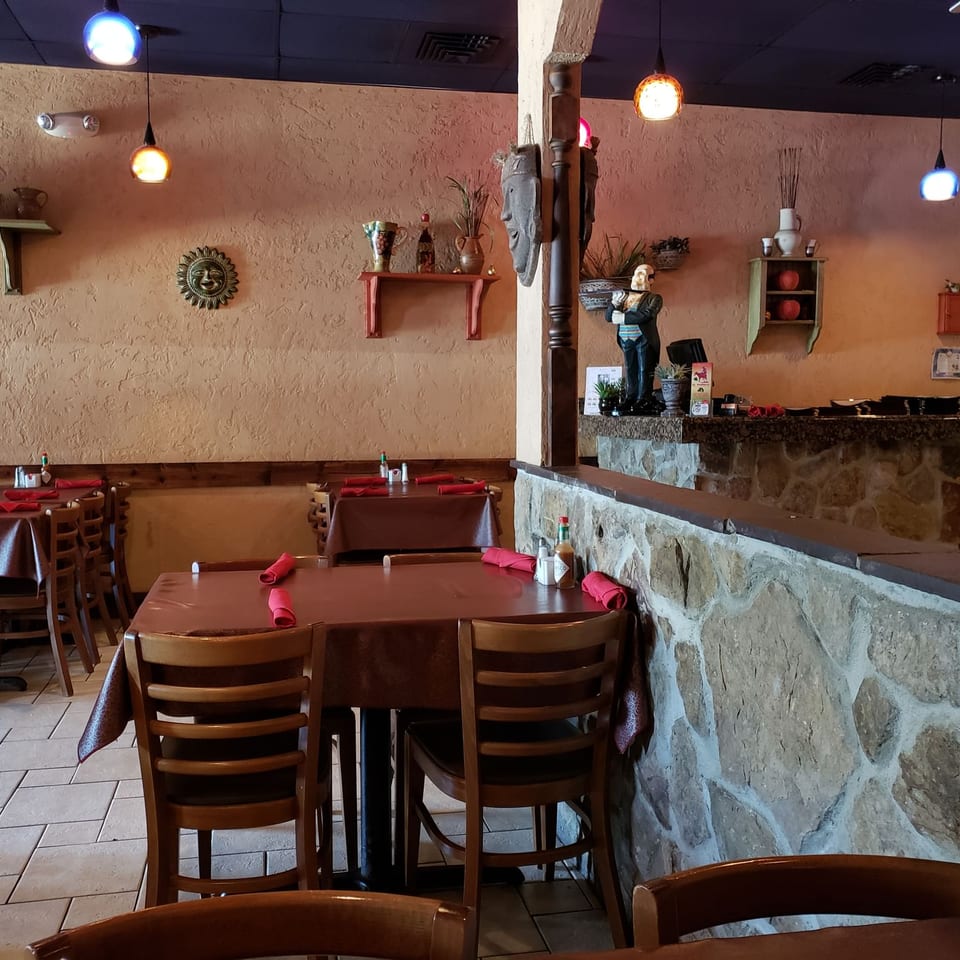Warmly lit restaurant dining room with red-clothed tables, colorful pendant lights, cultural decorations, and a stone service counter.